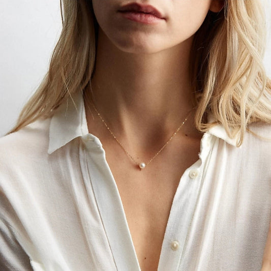 A person wearing a white shirt showcasing a gold-plated necklace with a single pearl pendant.
