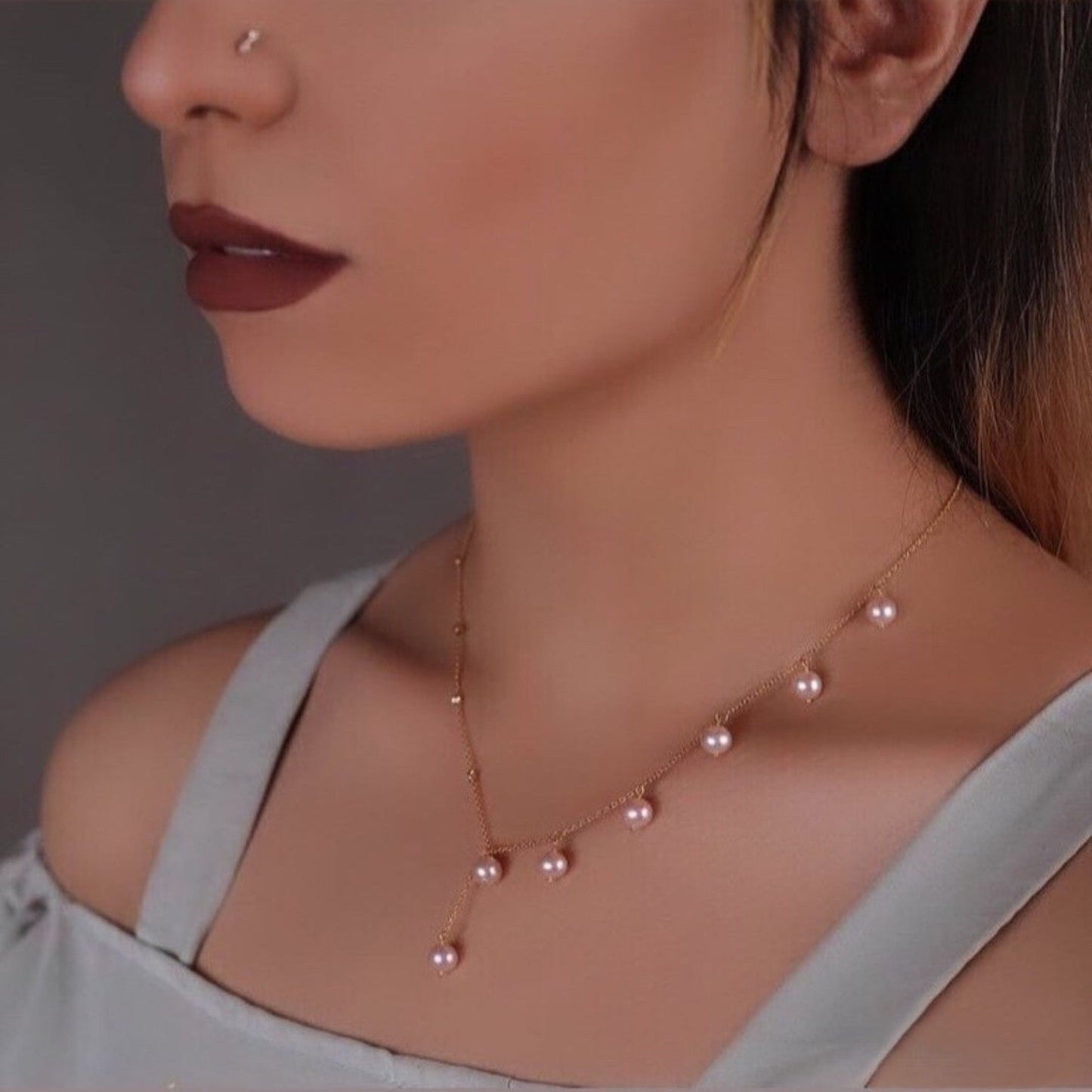 Woman wearing a delicate pearl necklace with a neutral background.