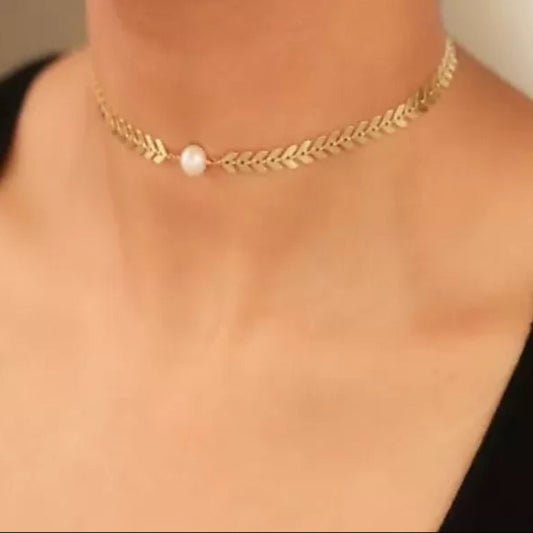 Gold necklace with a pearl pendant on a person wearing a black top.