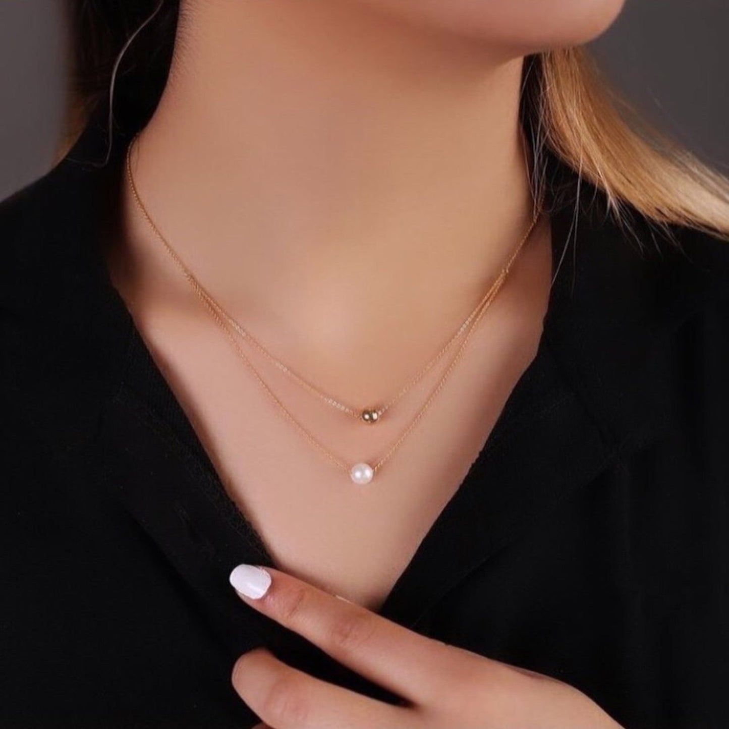 Woman wearing a delicate pearl necklace with a black top.