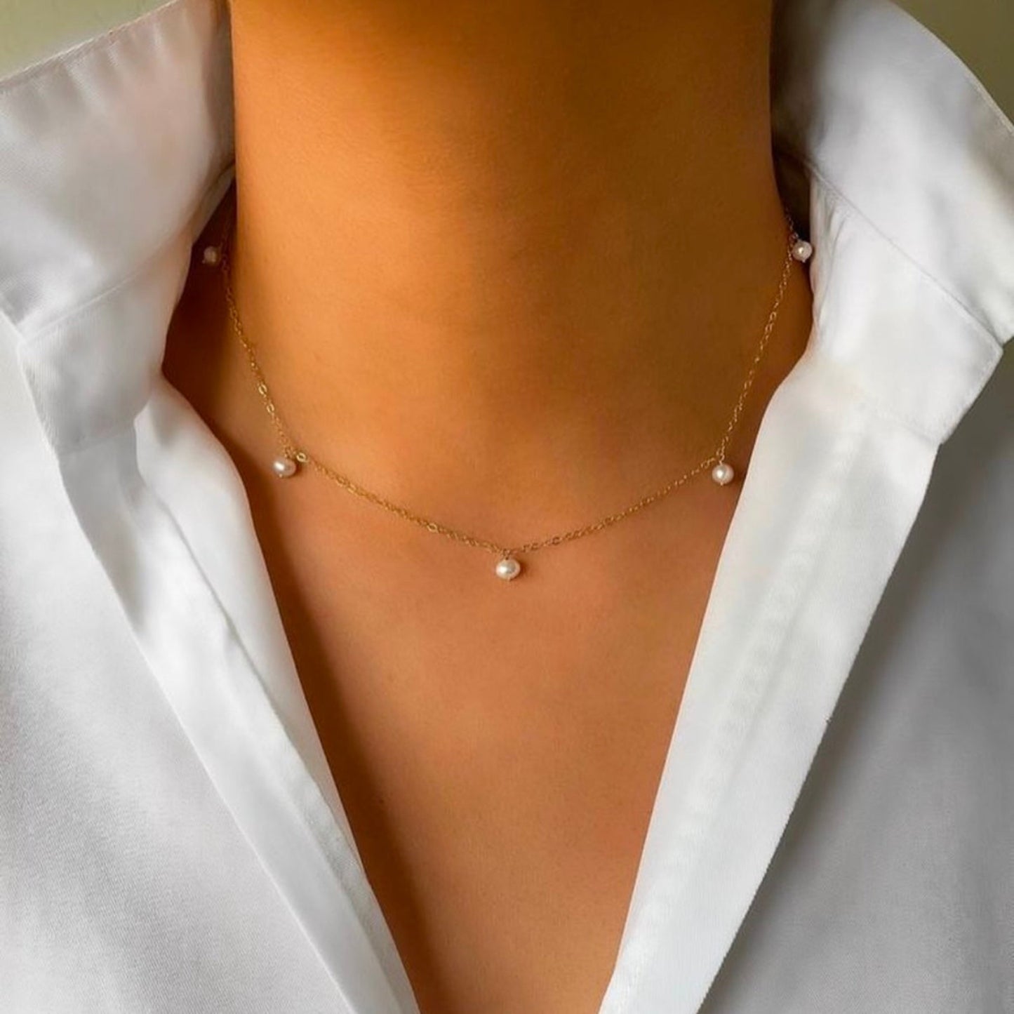 Gold necklace with pearls worn by a person in a white shirt