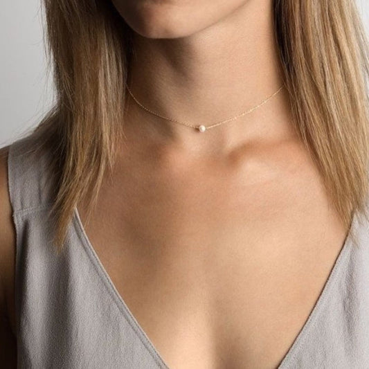 Necklace with a small pendant worn by a person with light skin and shoulder-length hair.