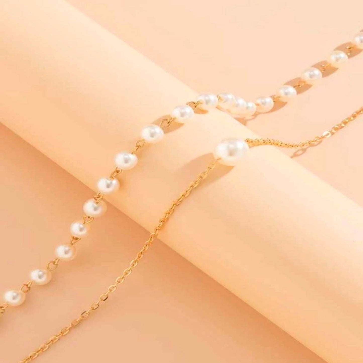 Gold chain with pearl beads on a peach-colored fabric background