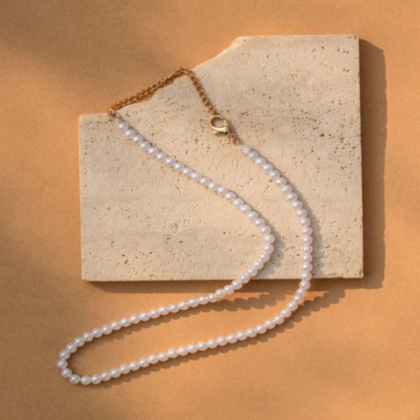 Pearl necklace with gold clasp on a stone surface with a warm brown background