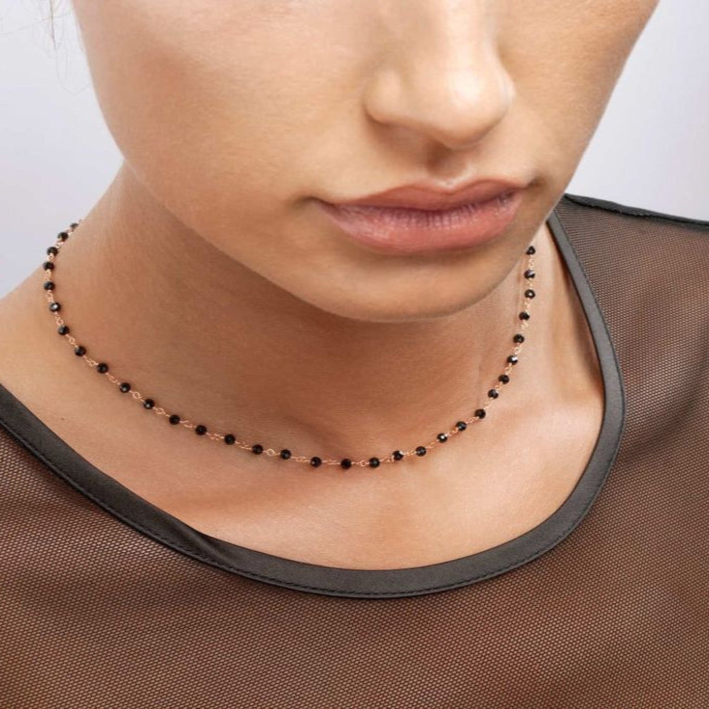 Close-up of a person wearing a delicate necklace with a neutral background
