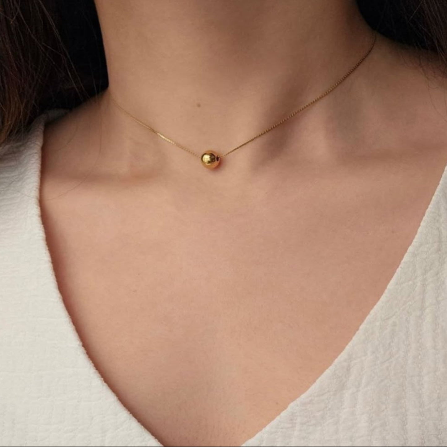 Gold necklace with a round pendant on a person wearing a white top.