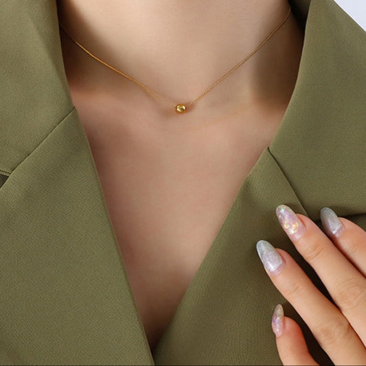 Gold necklace on a person wearing a green blazer with a hand touching the fabric.