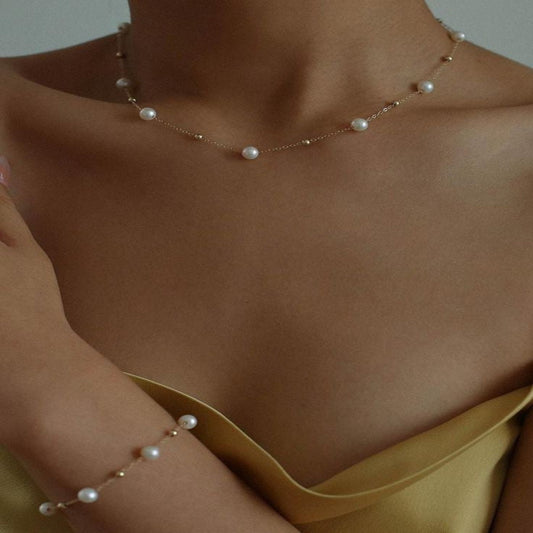 Pearl necklace and bracelet on a person wearing a yellow top against a neutral background