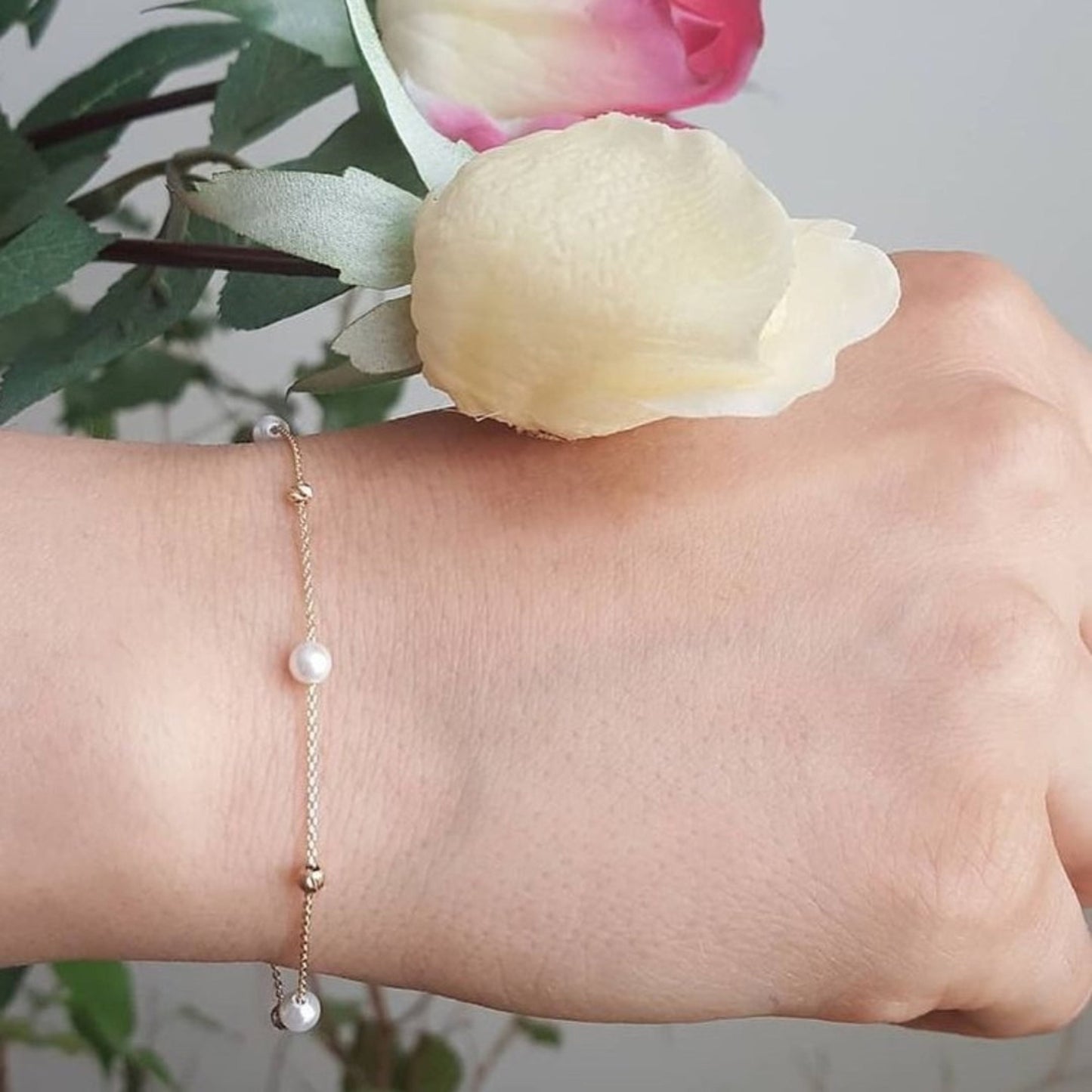 Hand wearing a pearl bracelet with a blurred floral background