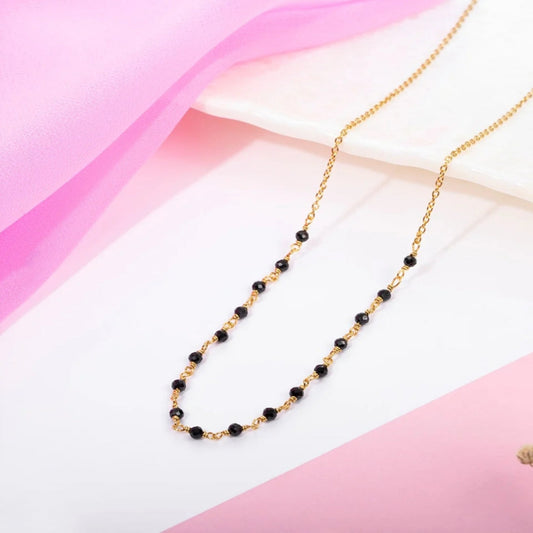 Gold necklace with black beads on a pink and white gradient background