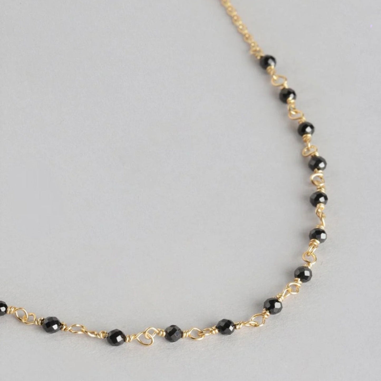Necklace with black beads and gold chain on a gray background