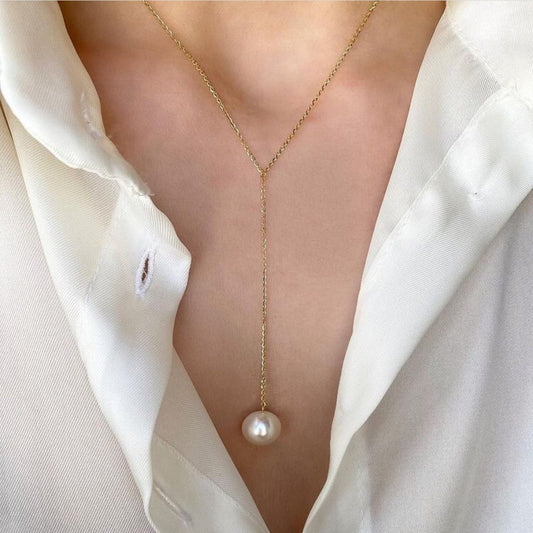 Gold necklace with a pearl pendant worn by a person in a white shirt.