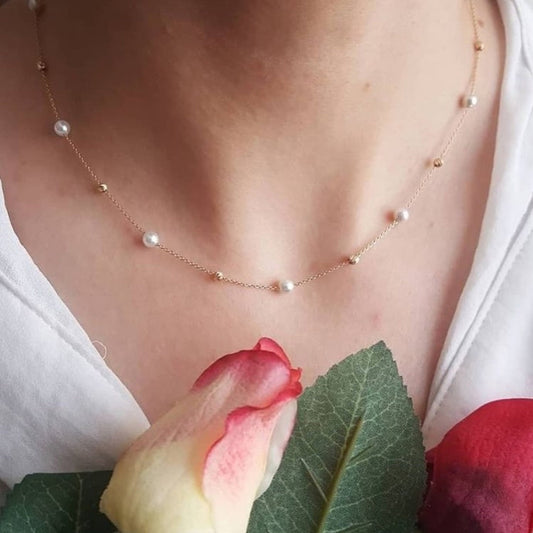 Necklace with small pearls worn by a person, with a white shirt and red flower in the background.
