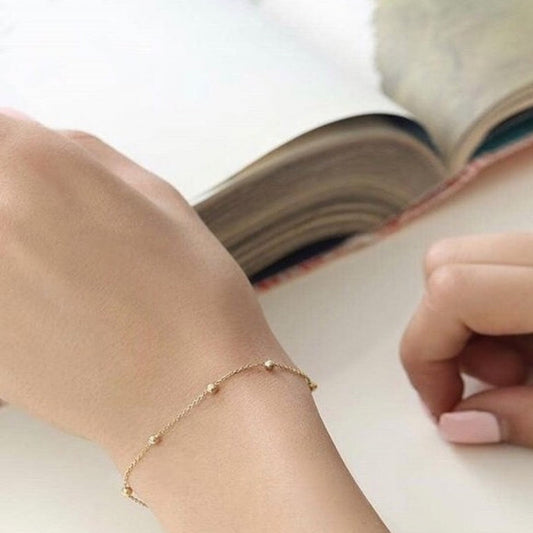 Close-up of a hand wearing a gold bracelet on a white surface with an open book.