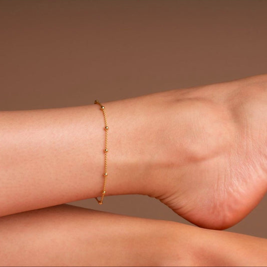 Gold anklet on a person's ankle against a brown background