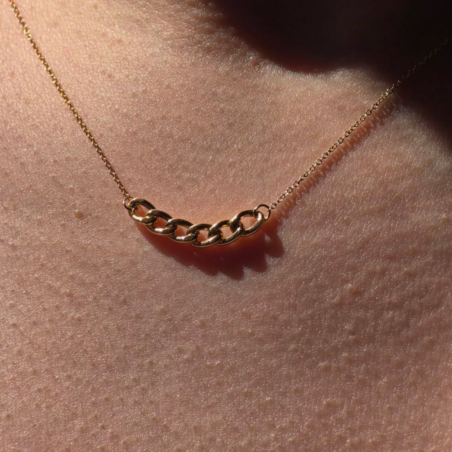 Gold chain necklace on a person's neck with a warm glow