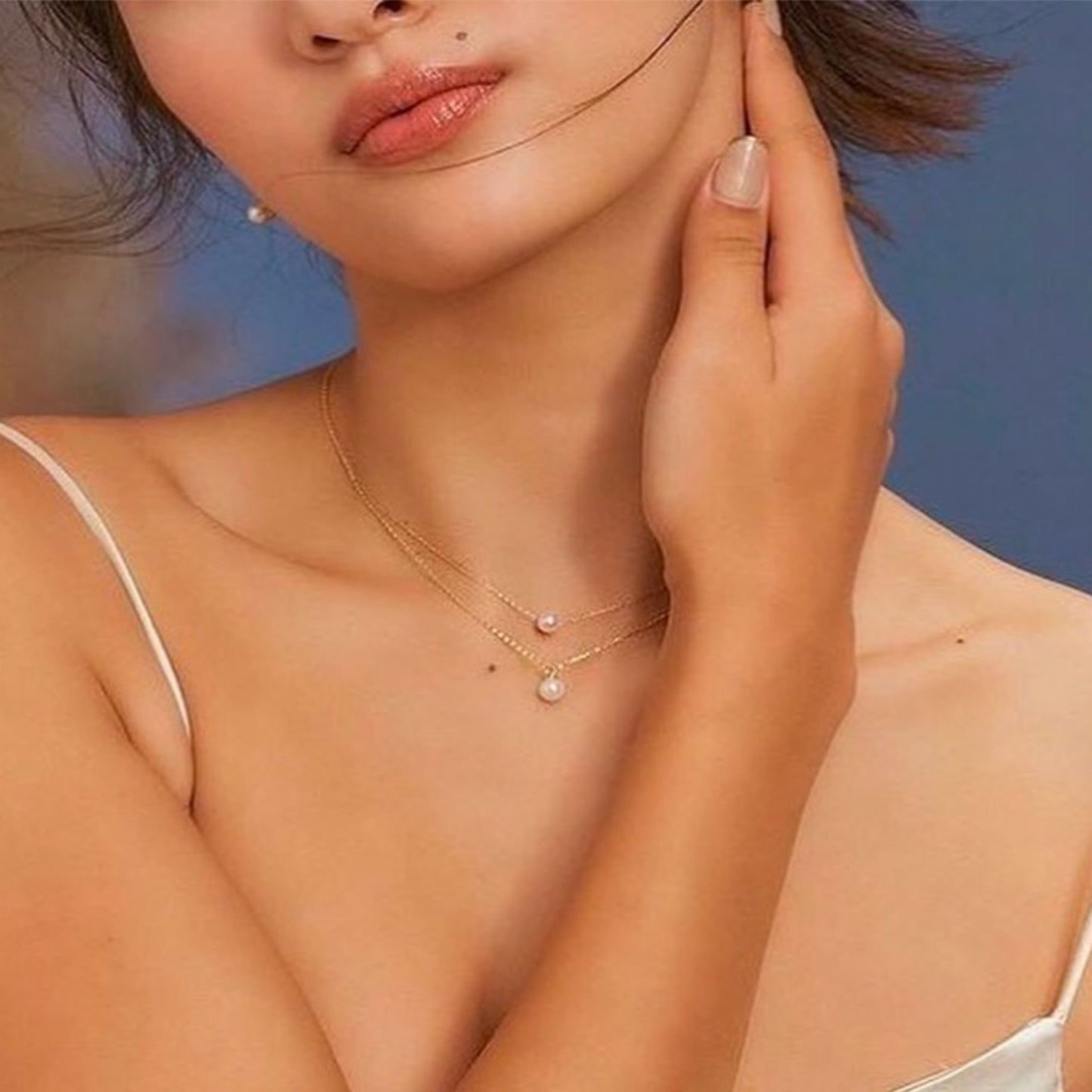 Woman wearing a delicate gold necklace with pearl pendants against a blue background
