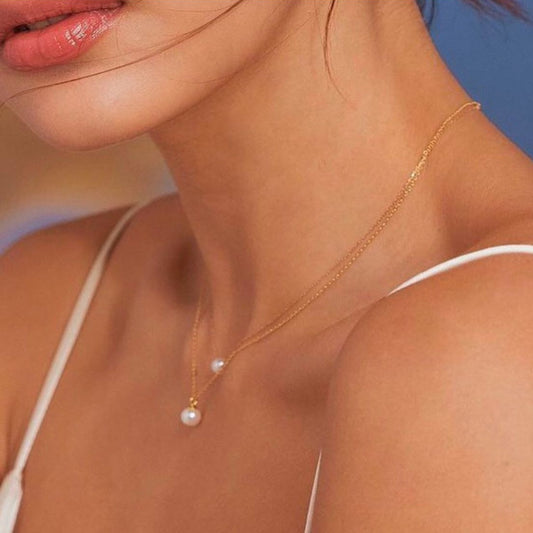 Close-up of a woman wearing a delicate gold necklace with pearls against a blue background