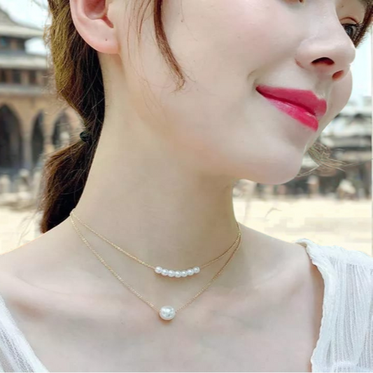 Close-up of a woman wearing gold necklaces with pearls against an outdoor background.