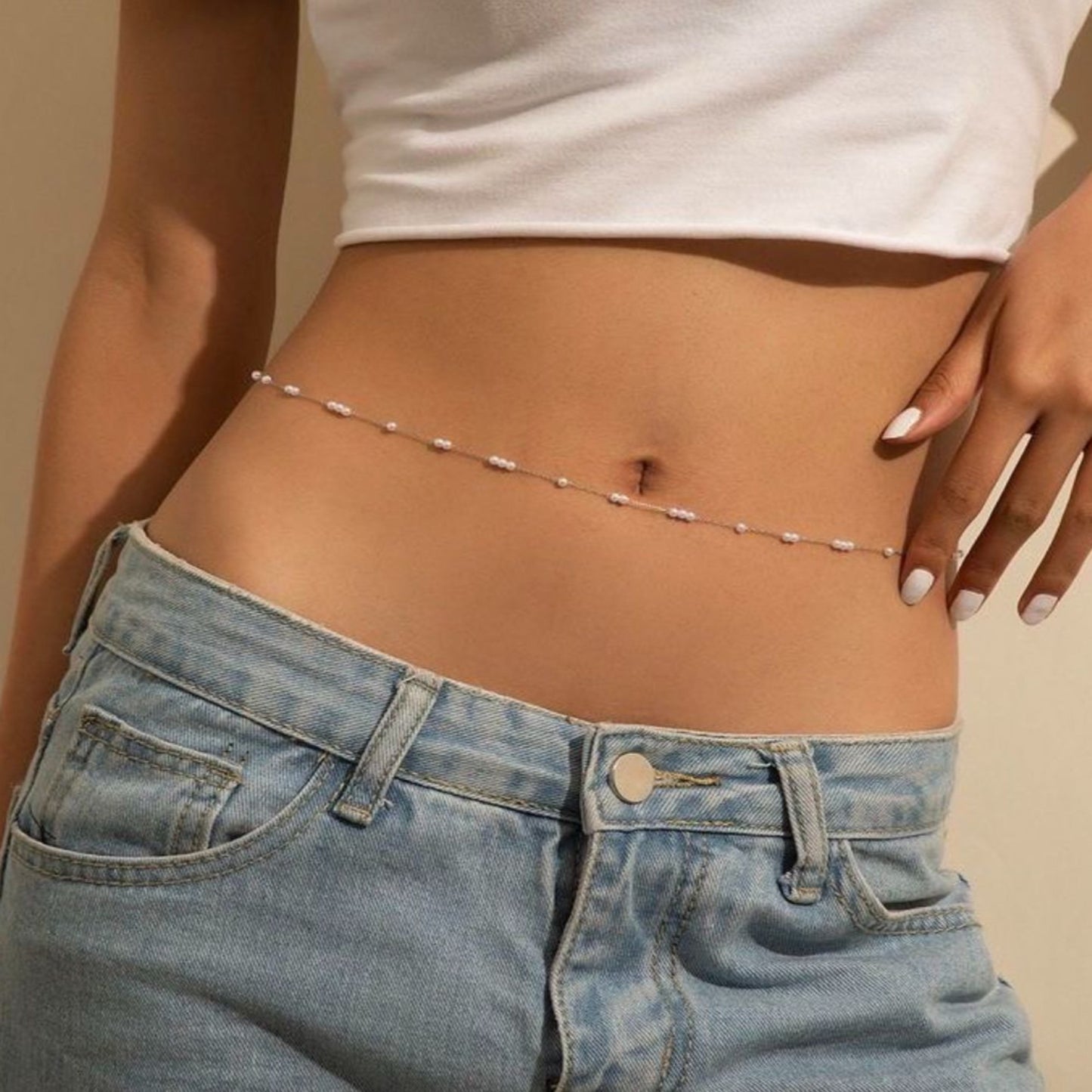 Person wearing a white top and blue jeans with a subtle chain around the waist on a beige background