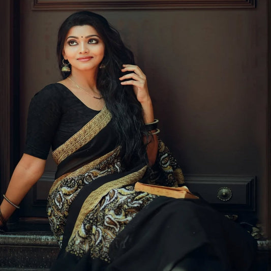 Woman in a black and gold saree sitting against a dark background
