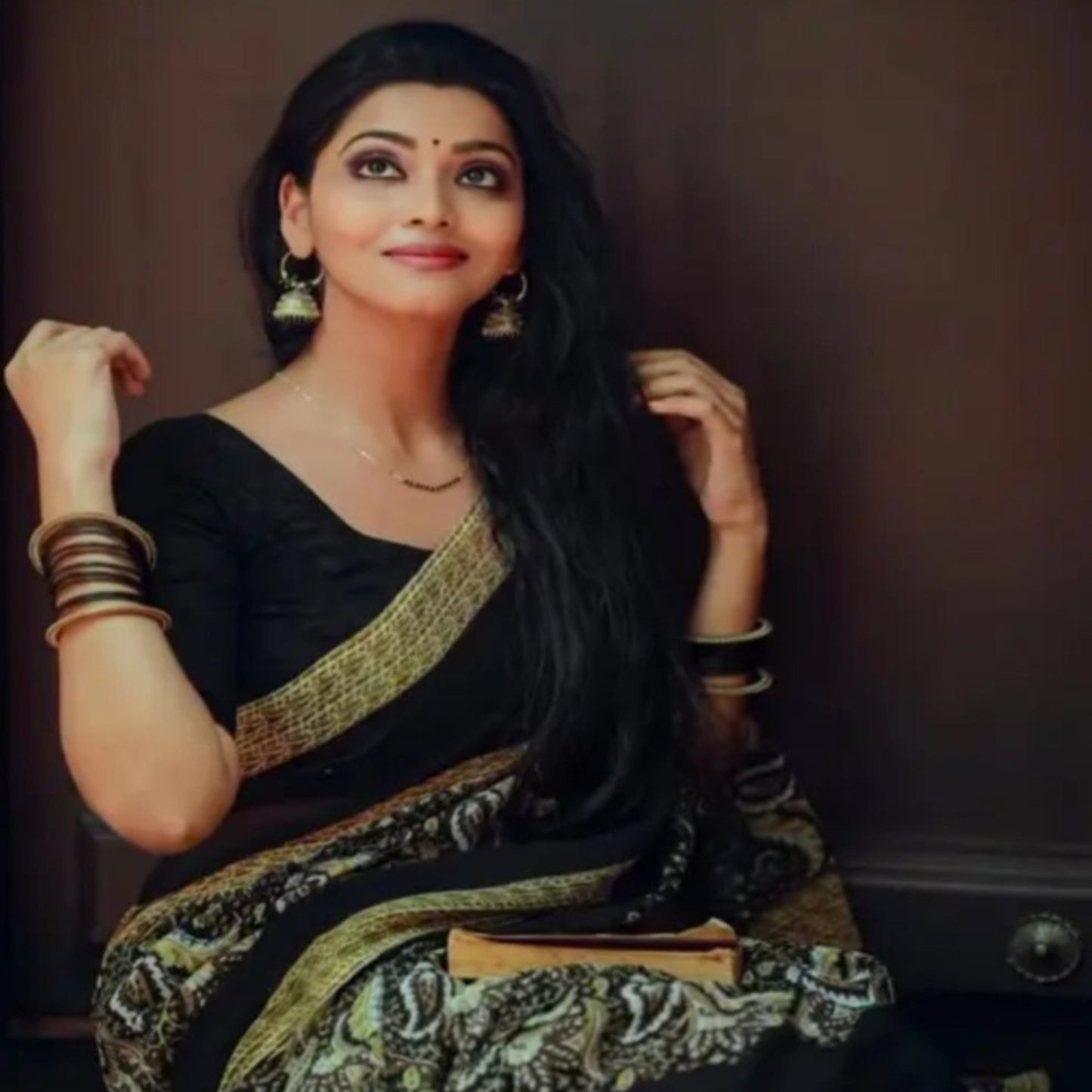 Woman in a black saree with gold patterns against a dark background