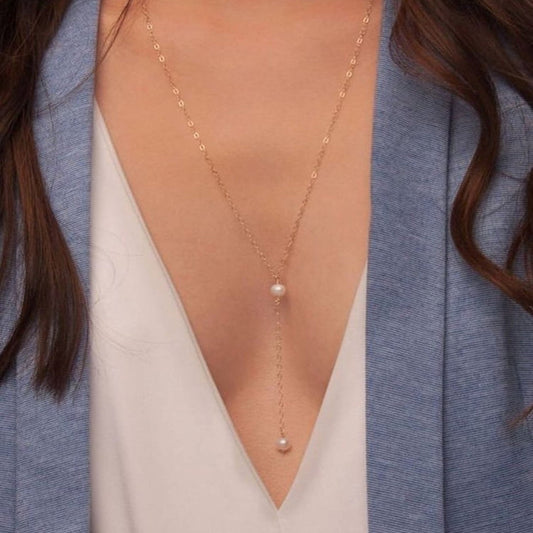Gold necklace with pearl pendant worn by a person in a blue cardigan and white top.