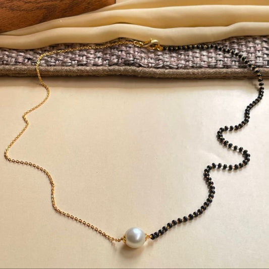 Necklace with gold chain, pearl, and black beads on a textured surface