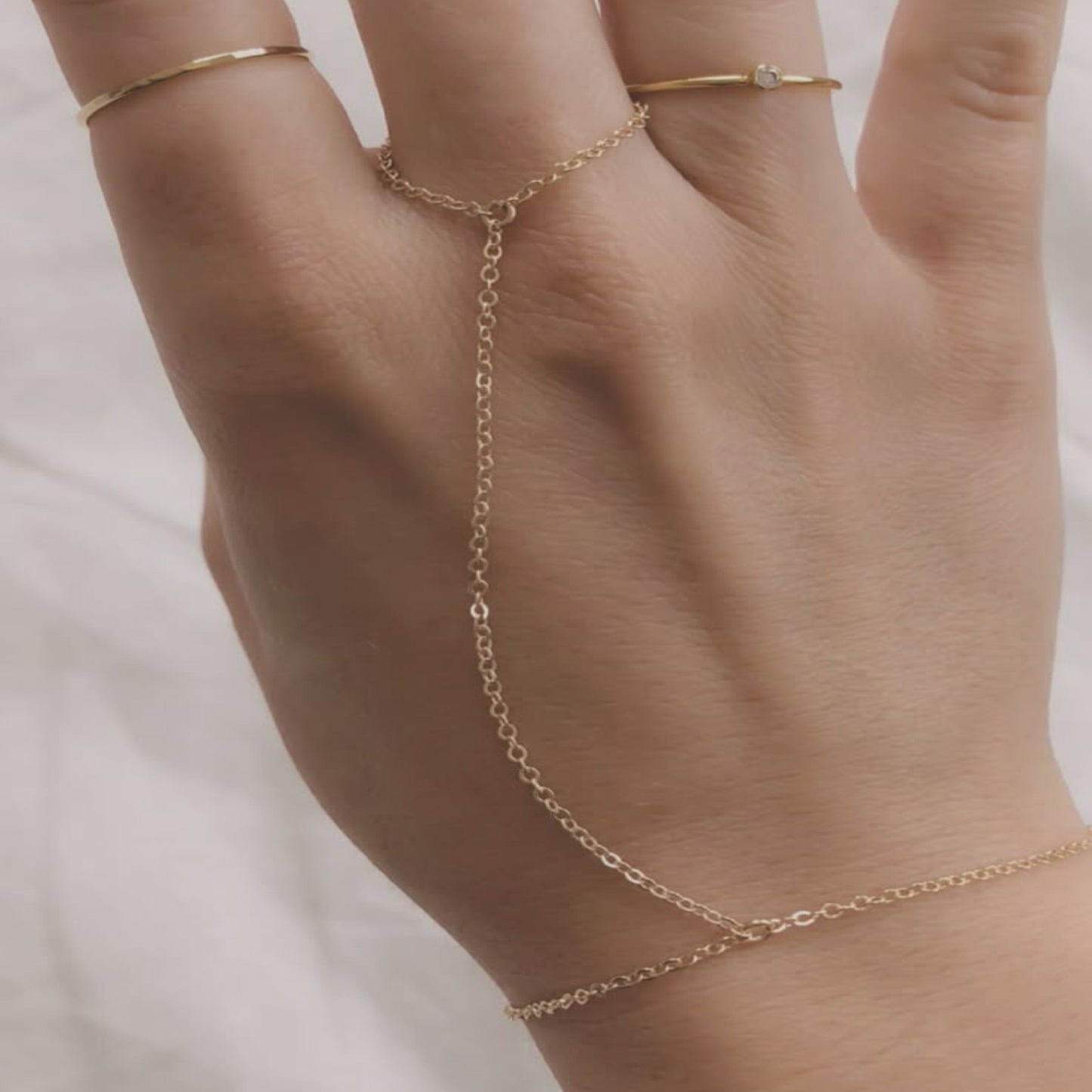 Hand wearing a delicate gold ring and bracelet on a neutral background