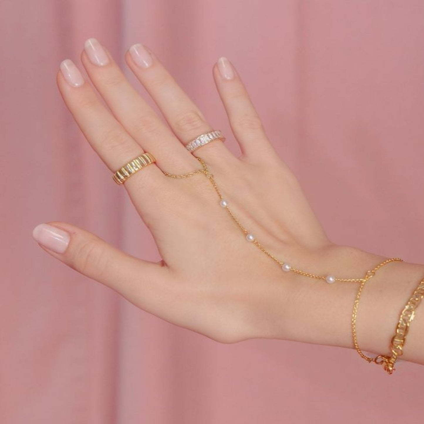 Hand wearing gold jewelry on a pink background