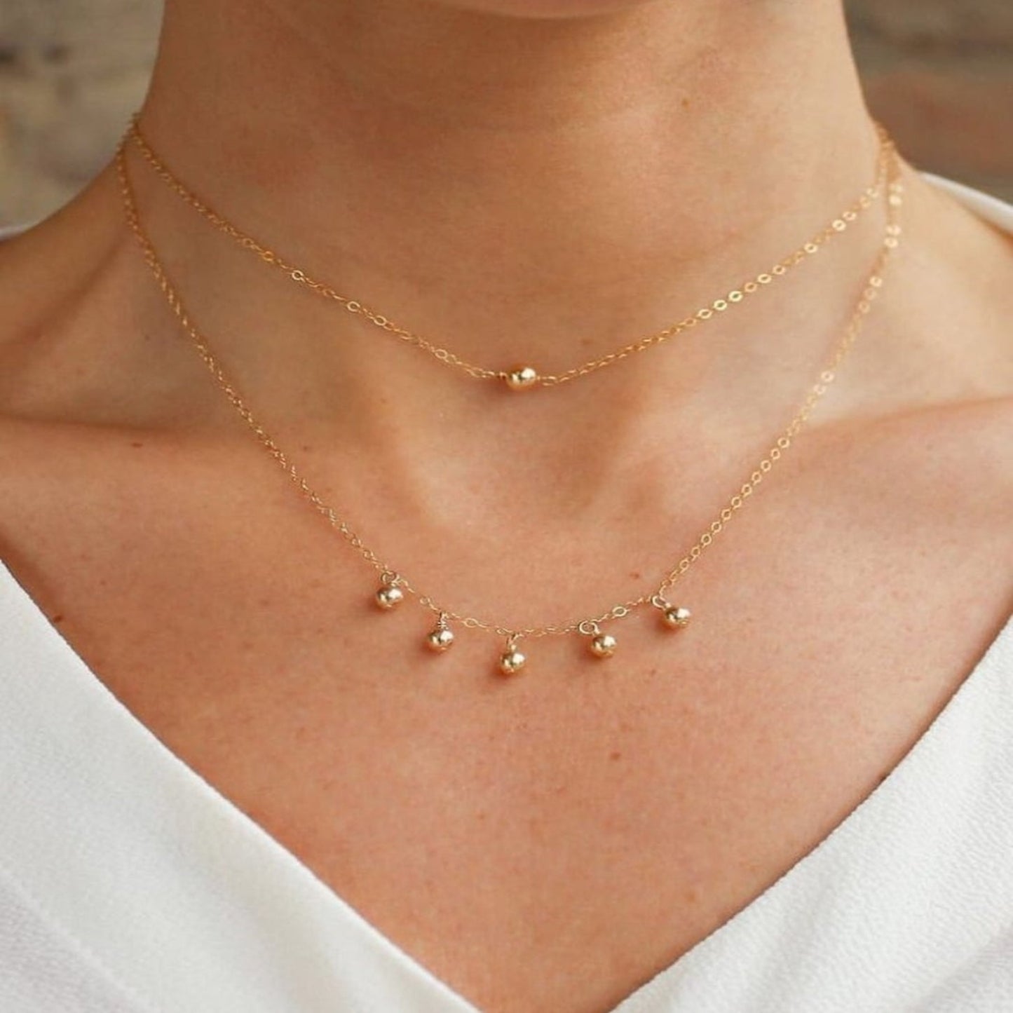 Gold necklace with small pendants on a person wearing a white top.