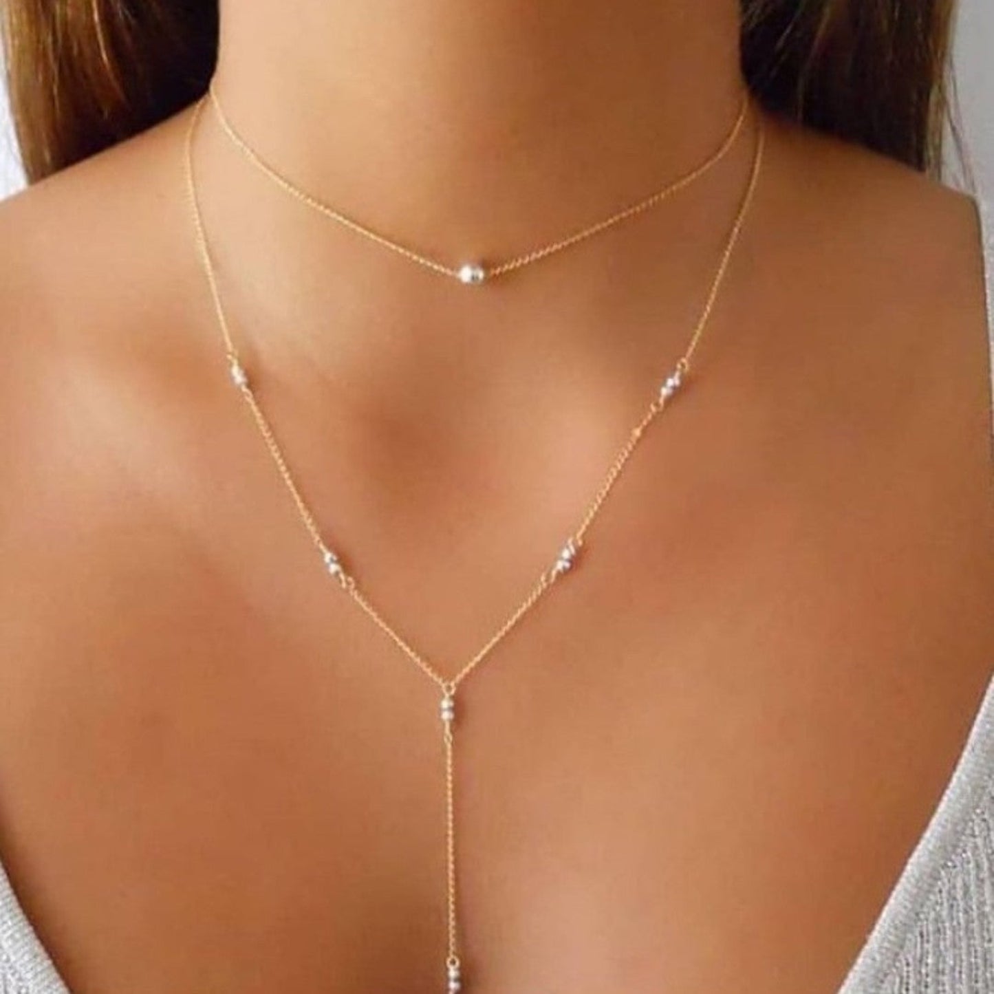 Gold necklace with small beads on a person wearing a gray top.