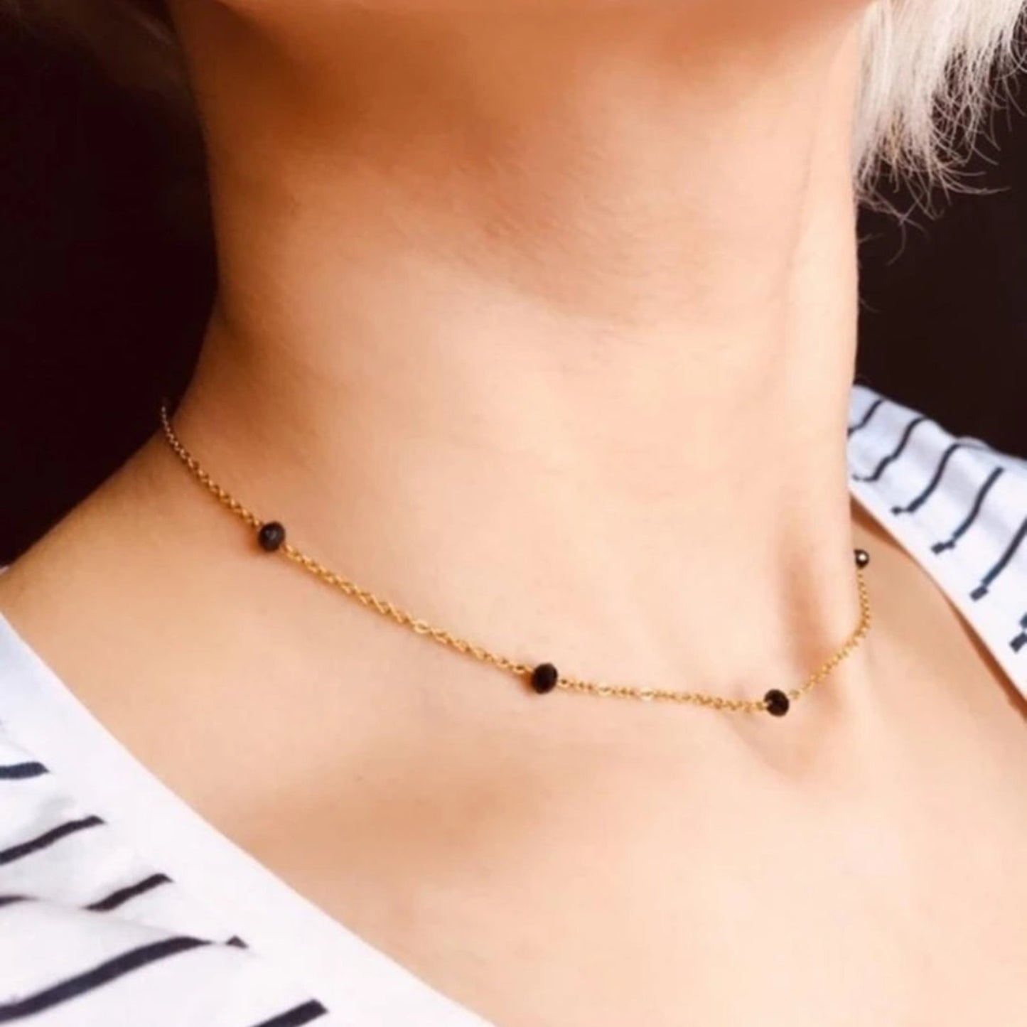 Gold necklace with black beads worn by a person