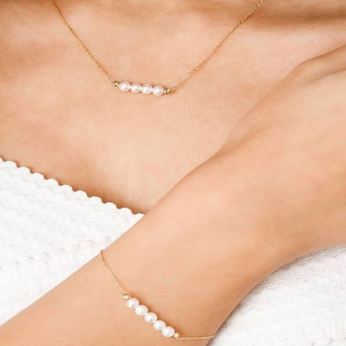 Gold necklace and bracelet with pearls on a person wearing a white lace garment.