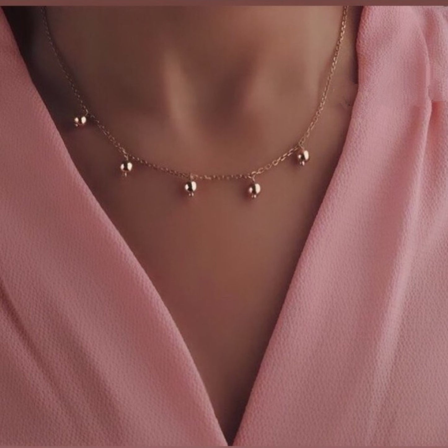 Gold necklace with small beads on a pink garment