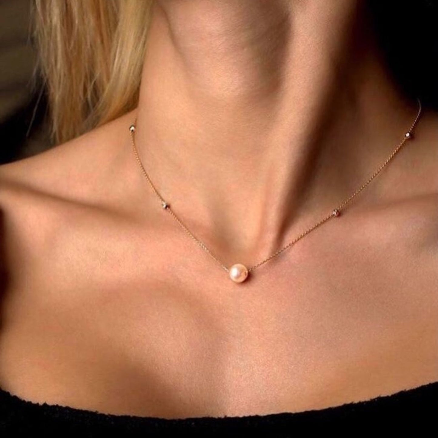 Necklace with a single pearl pendant on a person wearing a black top.