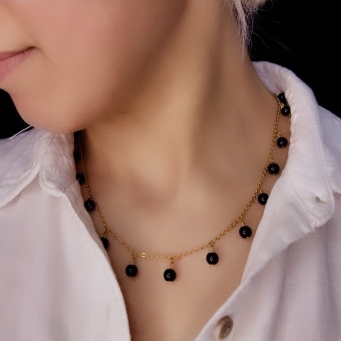 Necklace with black beads worn by a person against a white shirt background