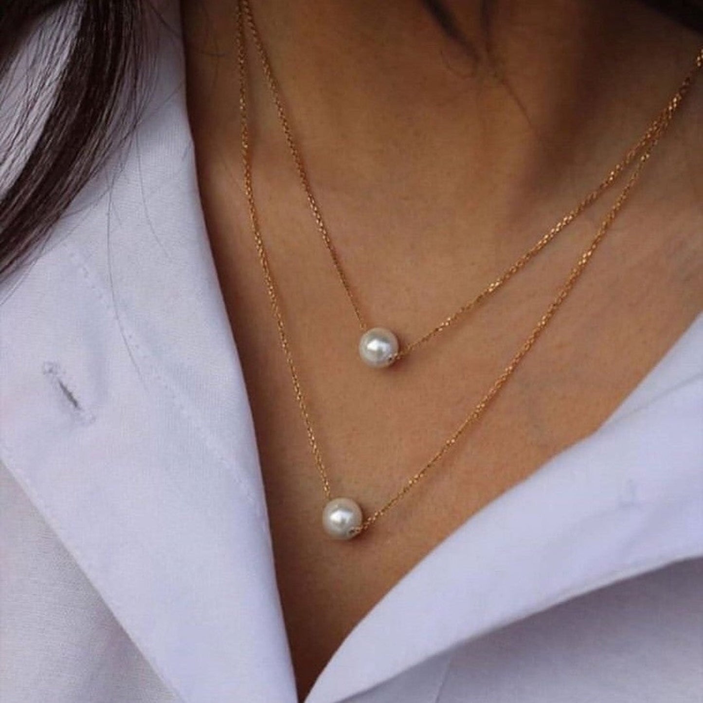 Two pearl necklaces on a person wearing a white shirt.