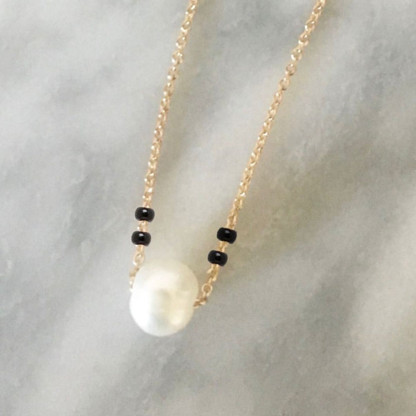 Necklace with a large pearl pendant and black beads on a light gray background