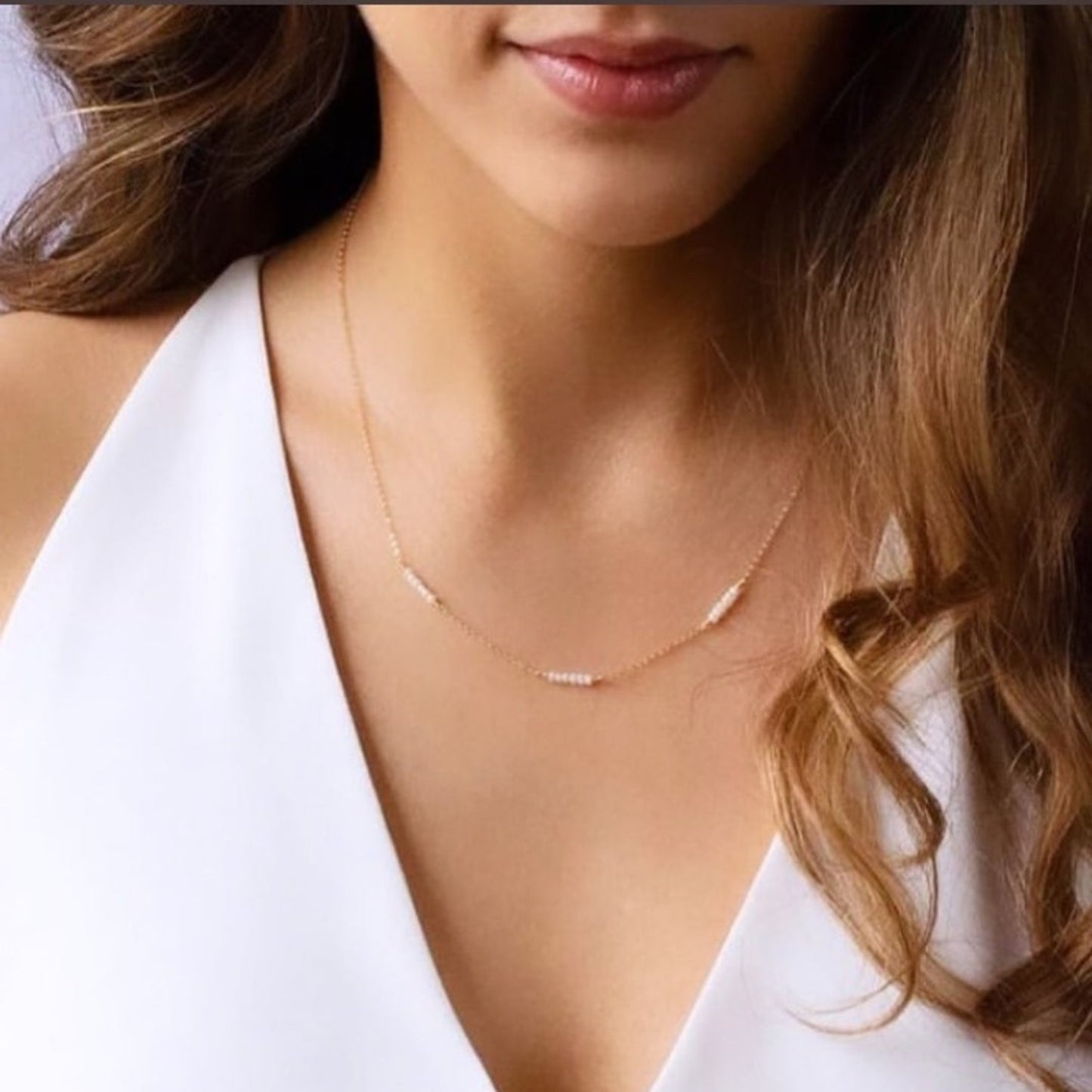 Close-up of a woman wearing a delicate gold necklace against a white background
