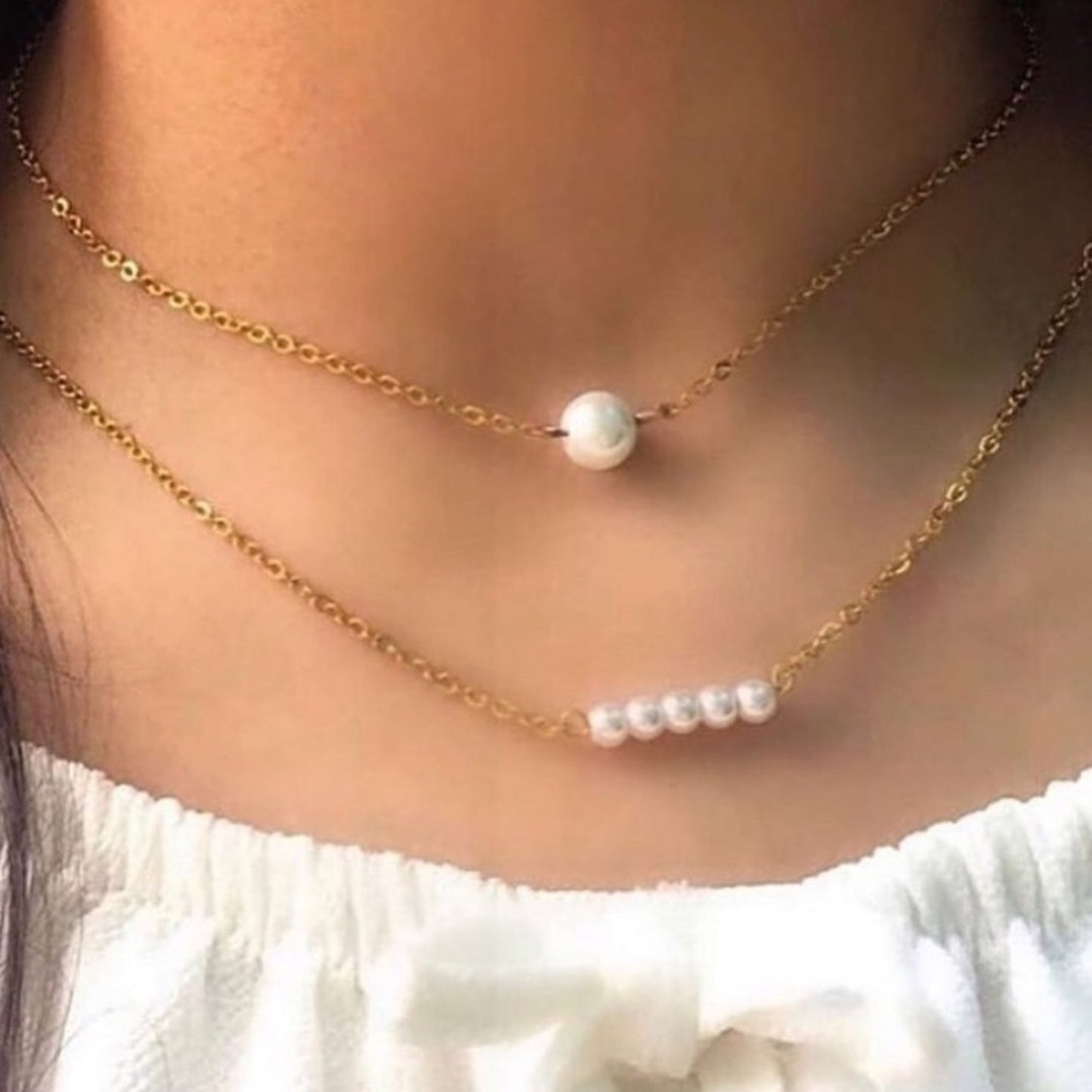 Two pearl necklaces on a person wearing a white top.