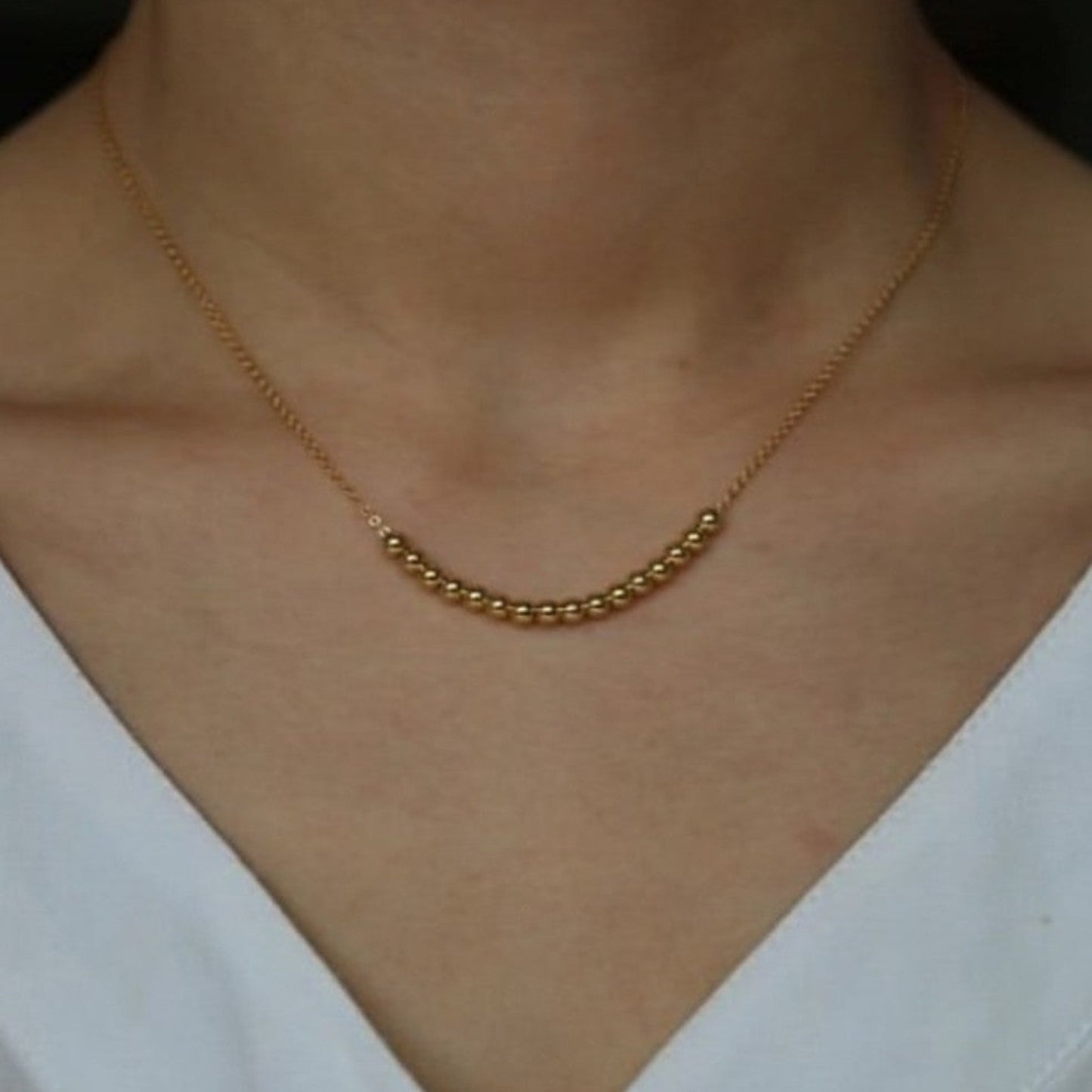 Gold necklace on a person wearing a white top