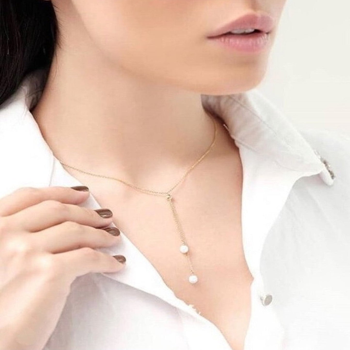 Person wearing a delicate gold necklace with small pearls on a white background