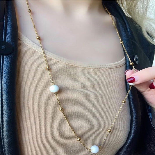 Gold necklace with white beads worn by a person