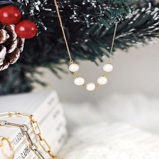 Pearl necklace with gold chain on a Christmas-themed background with pine cones and berries.