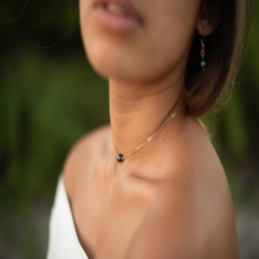 Close-up of a person wearing a delicate necklace with a blurred green background