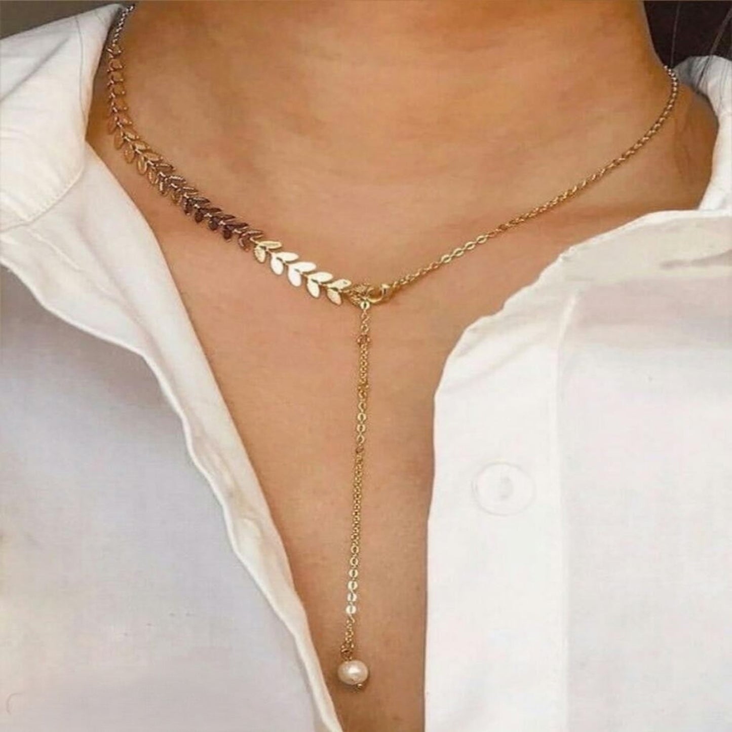 Gold chain necklace with a pearl pendant on a white shirt background