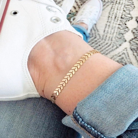 Gold chain bracelet on a person's wrist with a casual outfit.