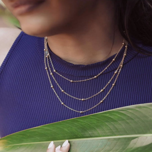 Person wearing a layered necklace with a blue top and green leaf in the foreground