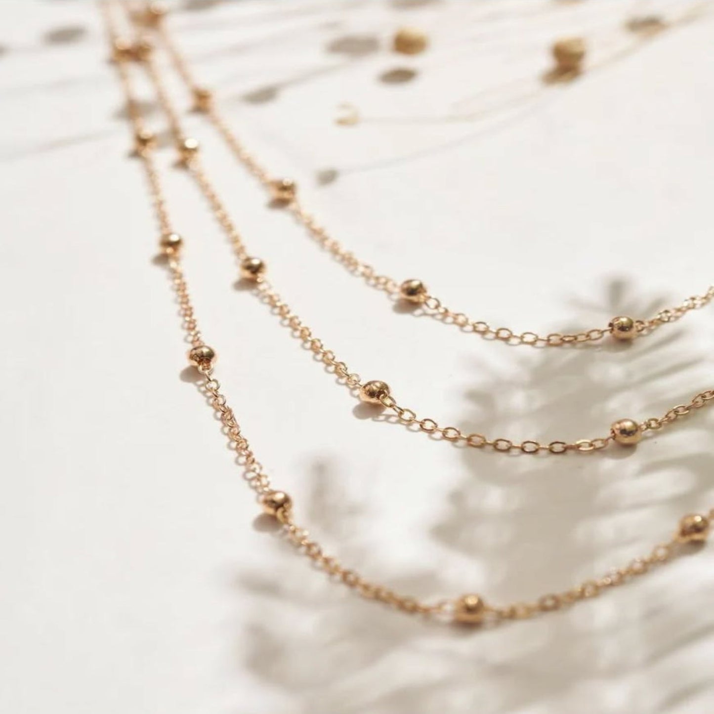 Two gold necklaces on a textured white surface